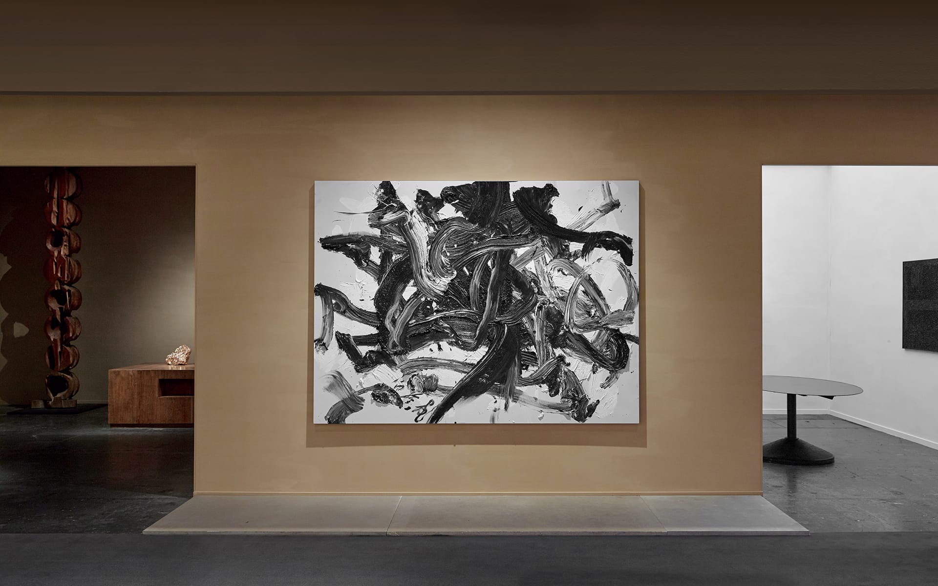 Abstract black and white painting displayed on a beige wall in a modern gallery setting.