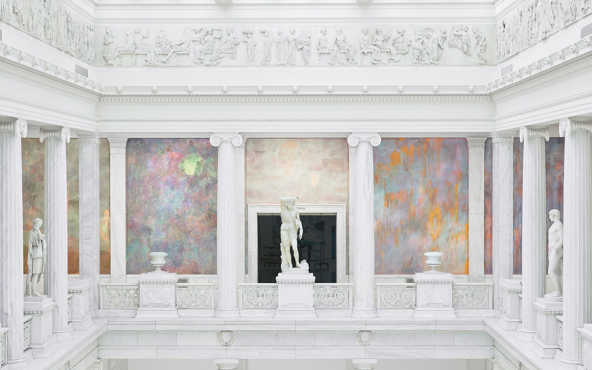 White marble museum interior with classical statues and colorful abstract murals on the walls.