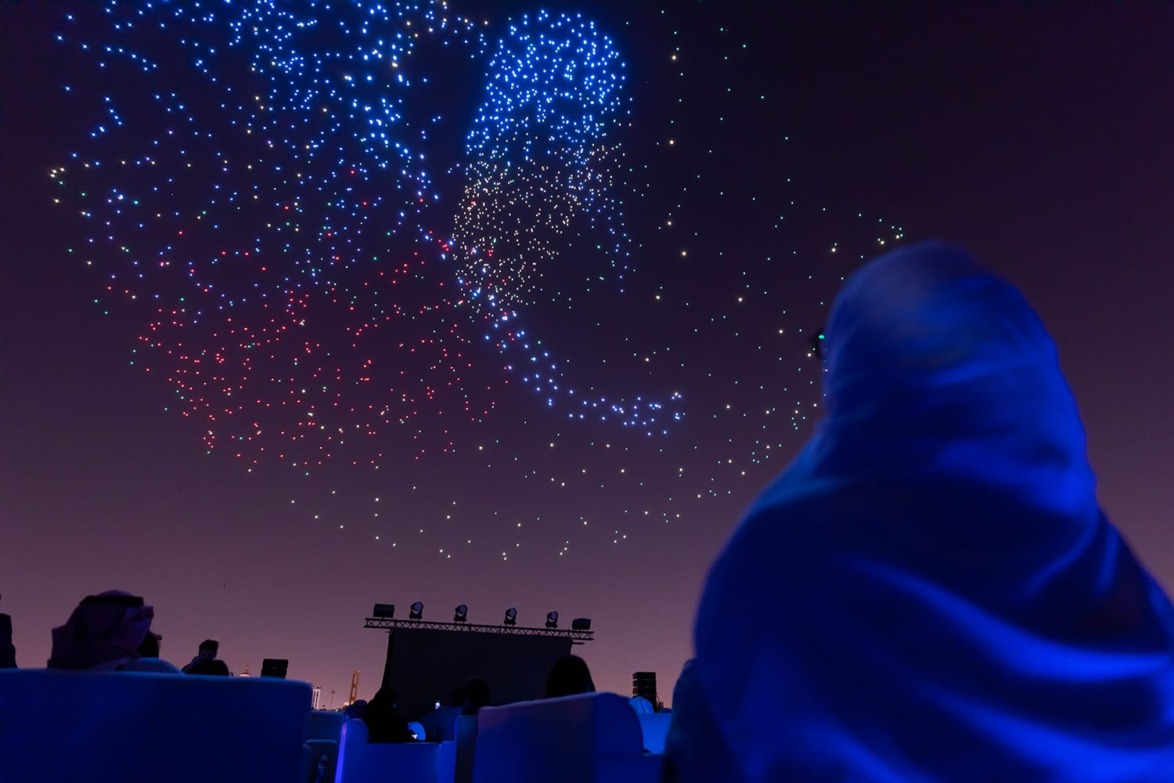 Silhouetted person watching colorful drone light show against night sky.