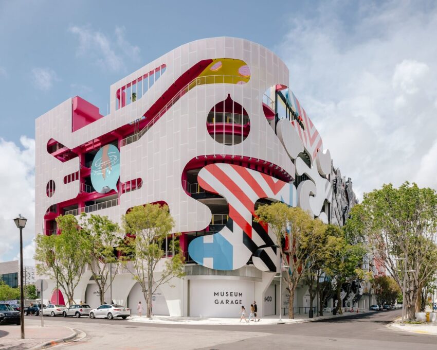 Colorful, architecturally diverse building facade with abstract designs, trees, and a street view on a sunny day.