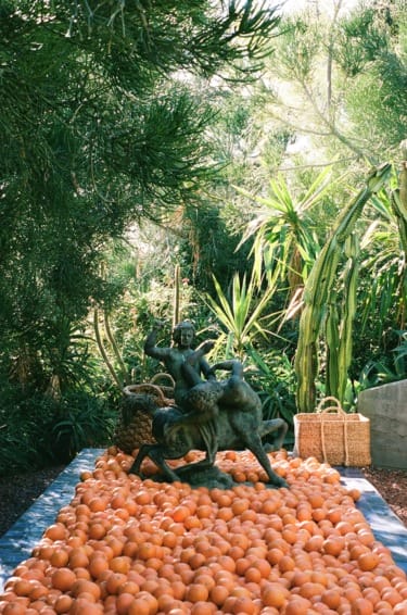 Outdoor display of fresh oranges with sculptures and greenery in the background.