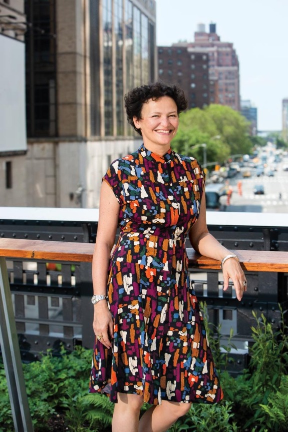 Person standing on a city balcony in a colorful dress, with buildings and a busy street in the background.
