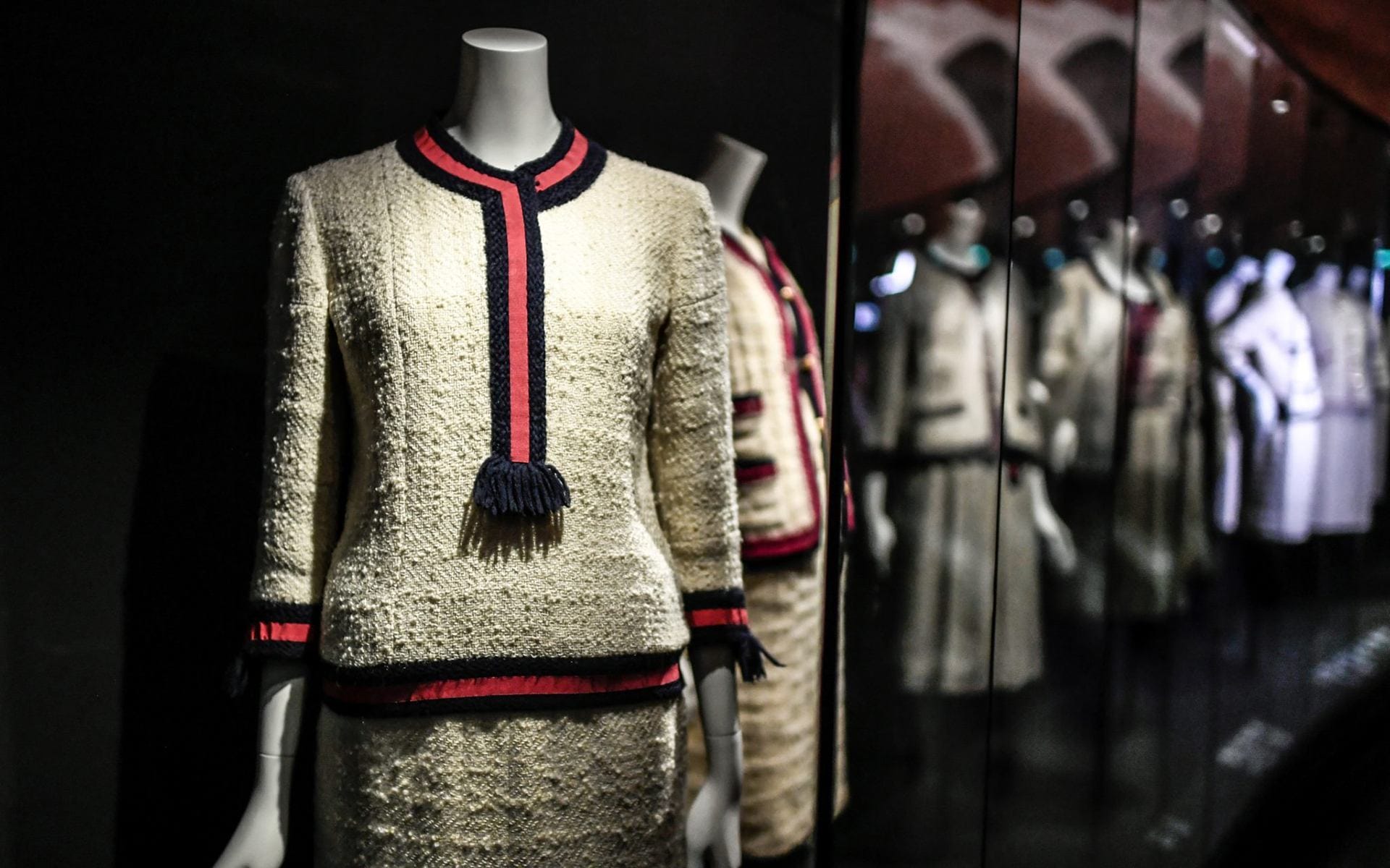 Mannequin displaying a textured cream outfit with red and black trim in a mirrored room.