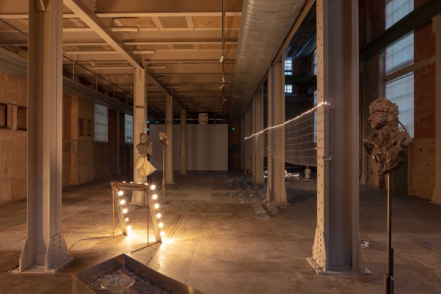 Industrial art installation with various sculptures, lights, and metallic structures inside a spacious, dimly lit warehouse.