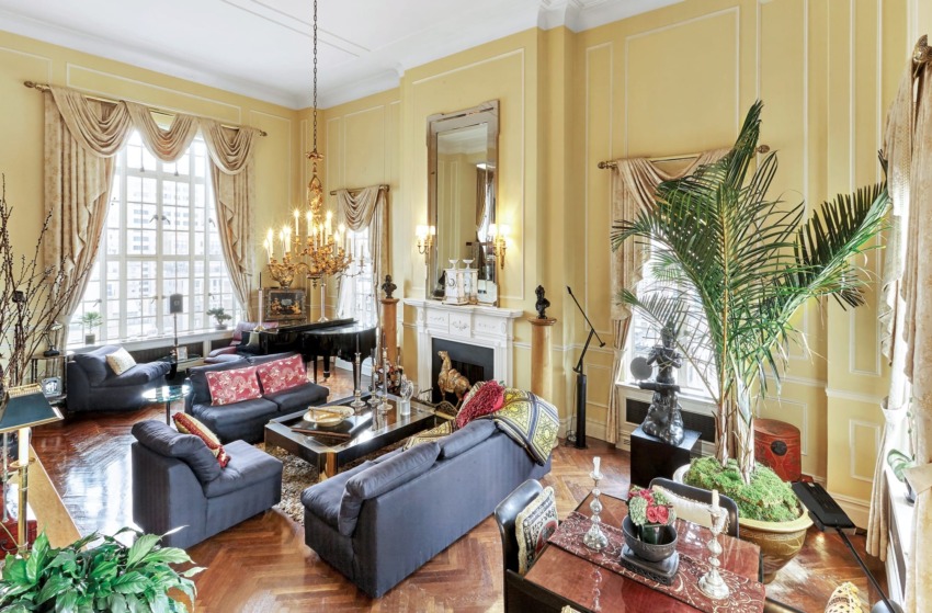 Elegant living room with yellow walls, grand piano, plush sofas, large windows, chandelier, and decorative plants.