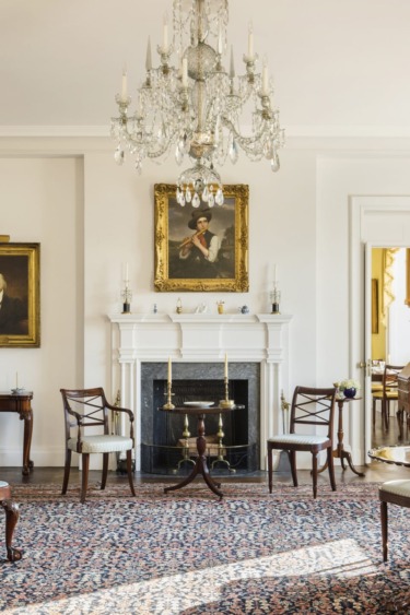 Elegant living room with chandelier, classic furniture, ornate rug, and paintings on the wall.