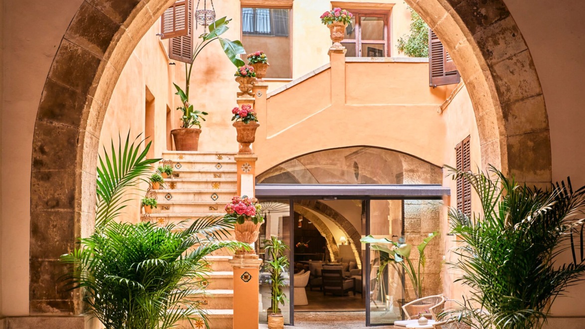 Mediterranean courtyard with stone archways, stairs adorned with potted plants, and a cozy seating area under soft lighting.