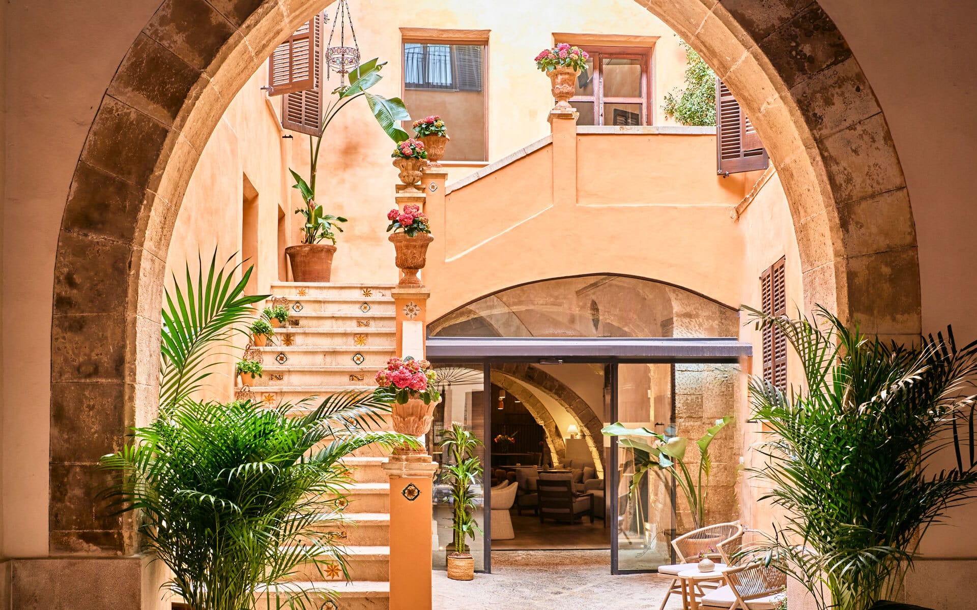 Mediterranean courtyard with stone archways, stairs adorned with potted plants, and a cozy seating area under soft lighting.