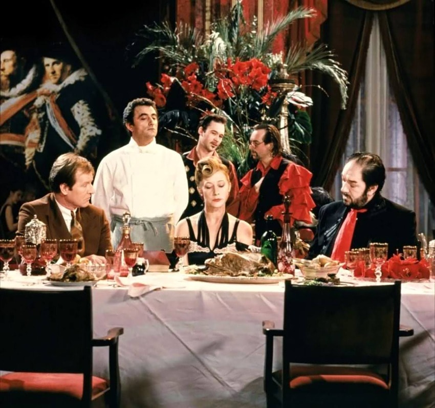 A group of people sitting around an elegant dinner table with red flowers and ornate decorations