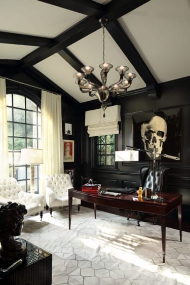 Elegant home office with dark walls, a chandelier, tufted chairs, large window, skull artwork, and a wooden desk.