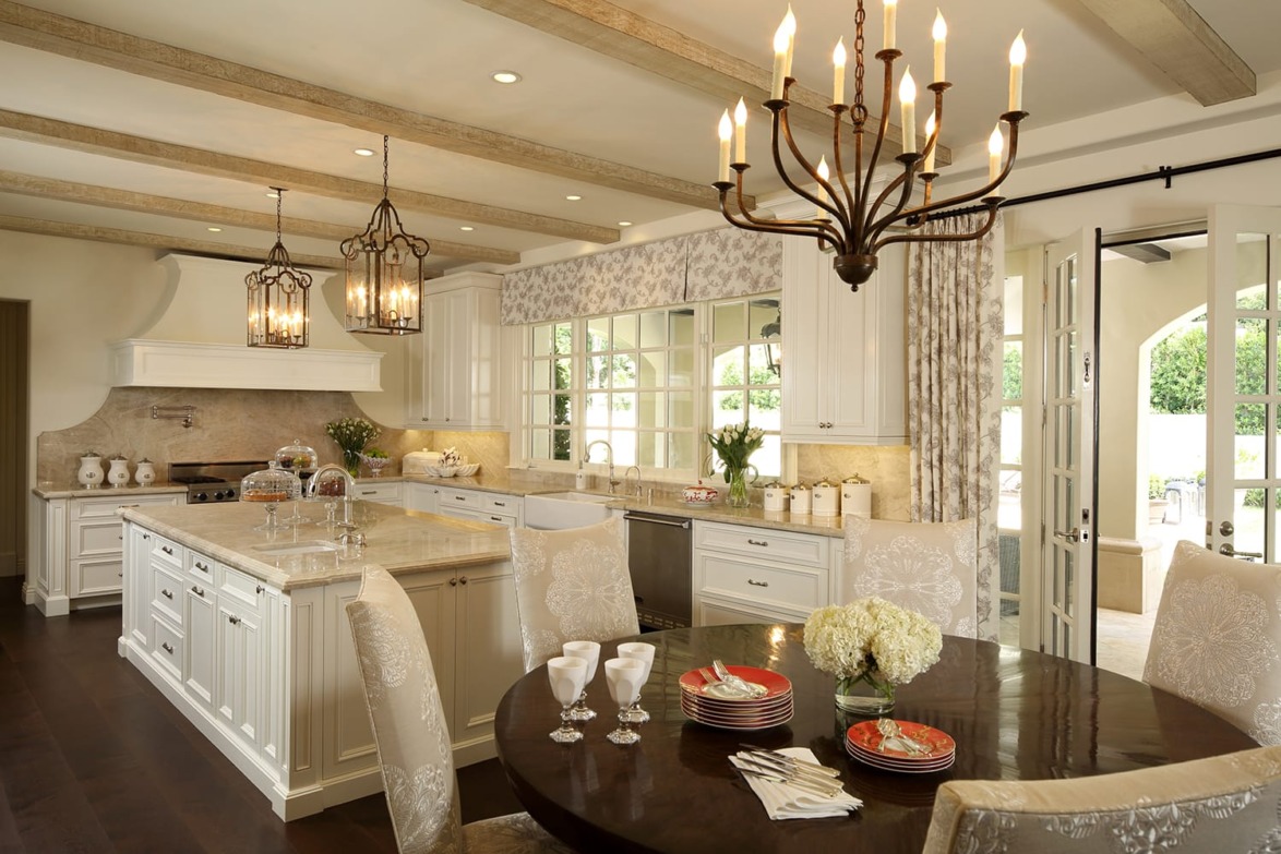 Elegant kitchen with white cabinetry, pendant lights, and a round dining table set for four under a rustic chandelier.