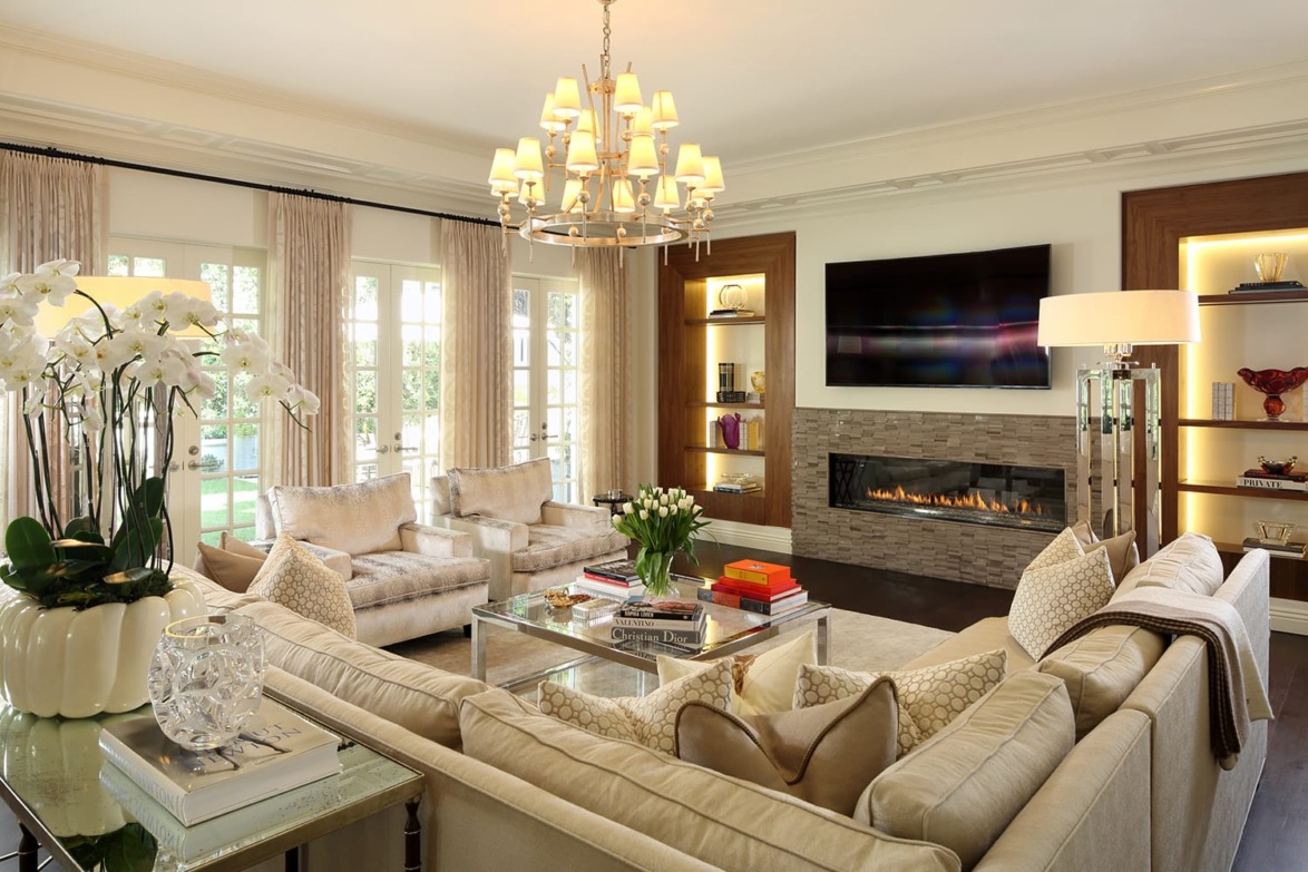 Luxurious living room with elegant chandelier, cozy fireplace, plush seating, large windows, and decorative shelves.