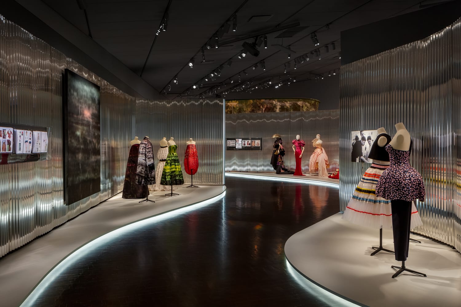 Museum exhibit with mannequins displaying colorful, avant-garde fashion pieces in a modern, well-lit gallery space.