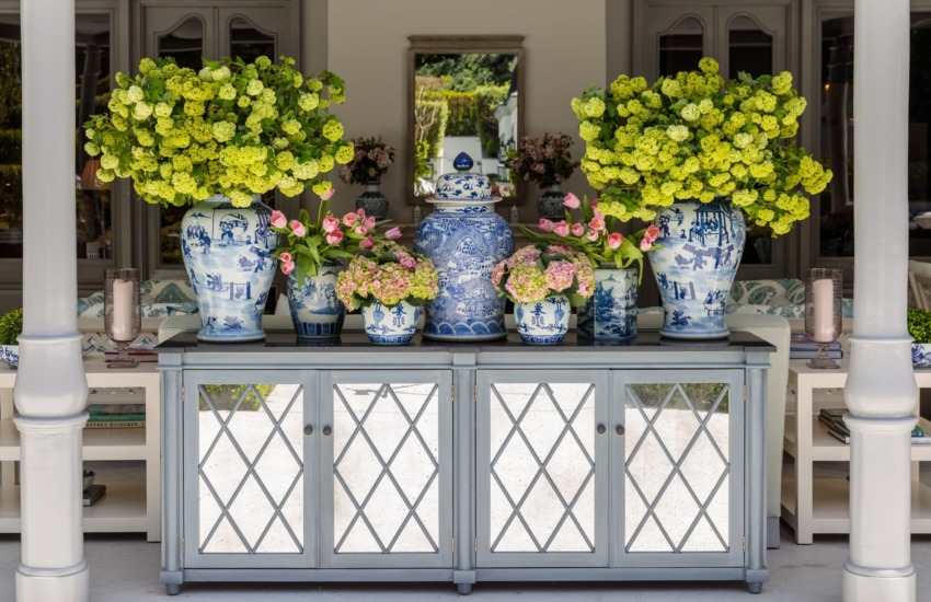 Elegant cabinet with mirrored doors decorated with large blue and white vases filled with green and pink flowers.