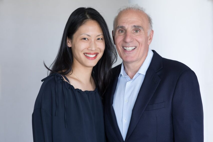 A smiling couple posing together in formal attire against a neutral background.