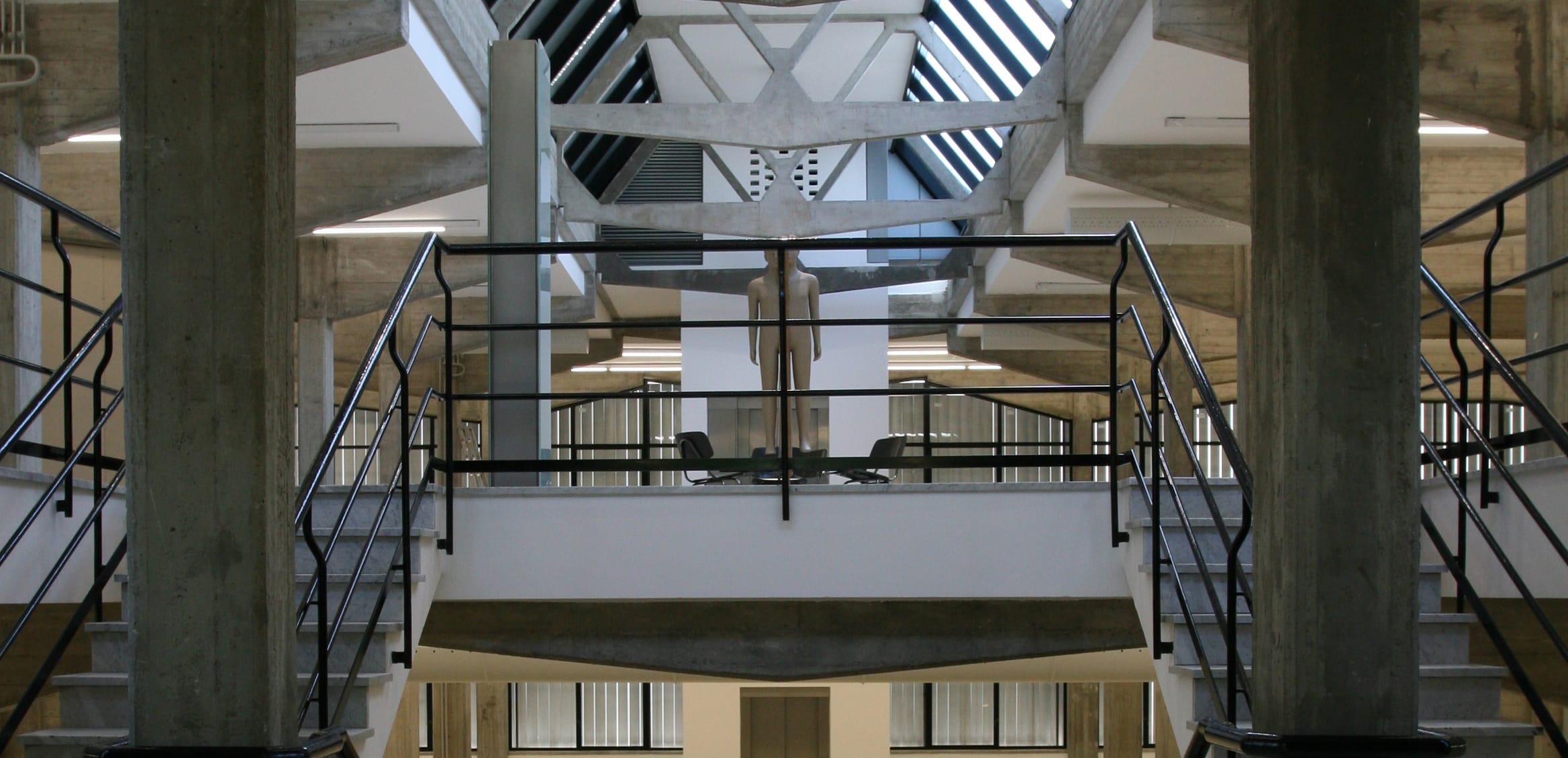 Interior of a modern building with concrete beams, metal railings, and skylights creating a bright, open space.