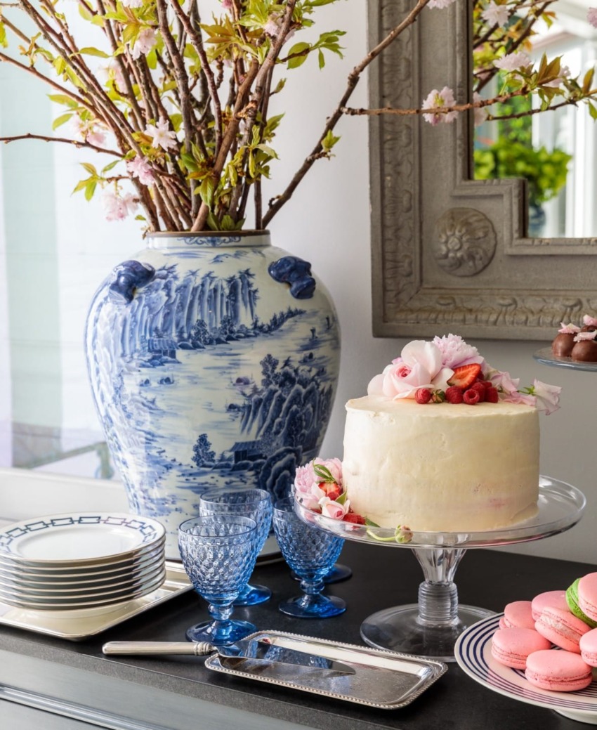 Elegant dessert display with a decorated cake, macarons, and a blue vase with flowers on a dining table.