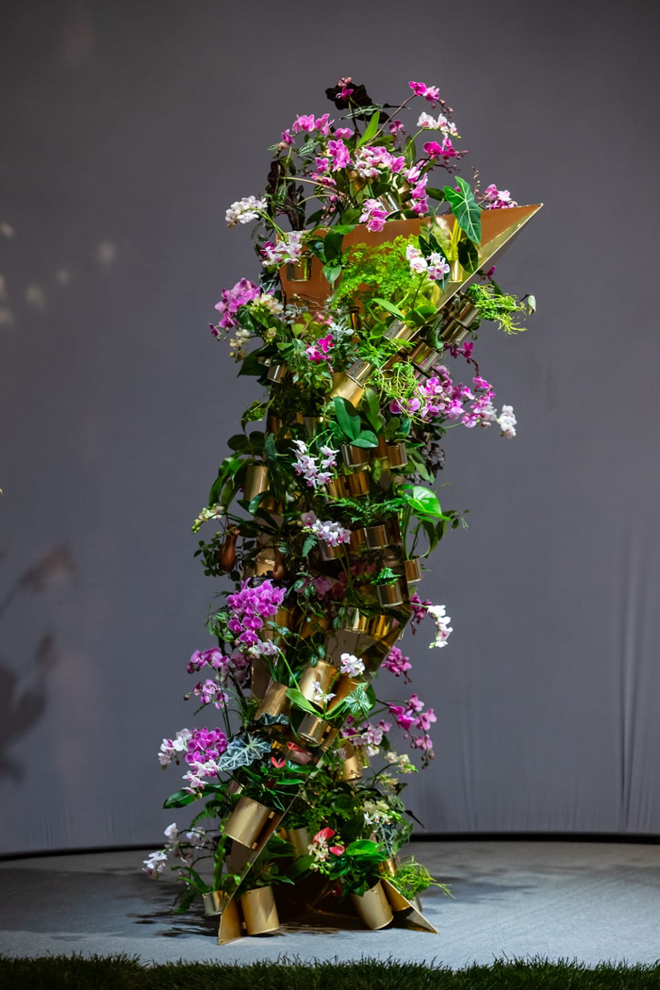 A tall floral arrangement entwined with pink and white flowers, showcased on a stage with soft lighting.