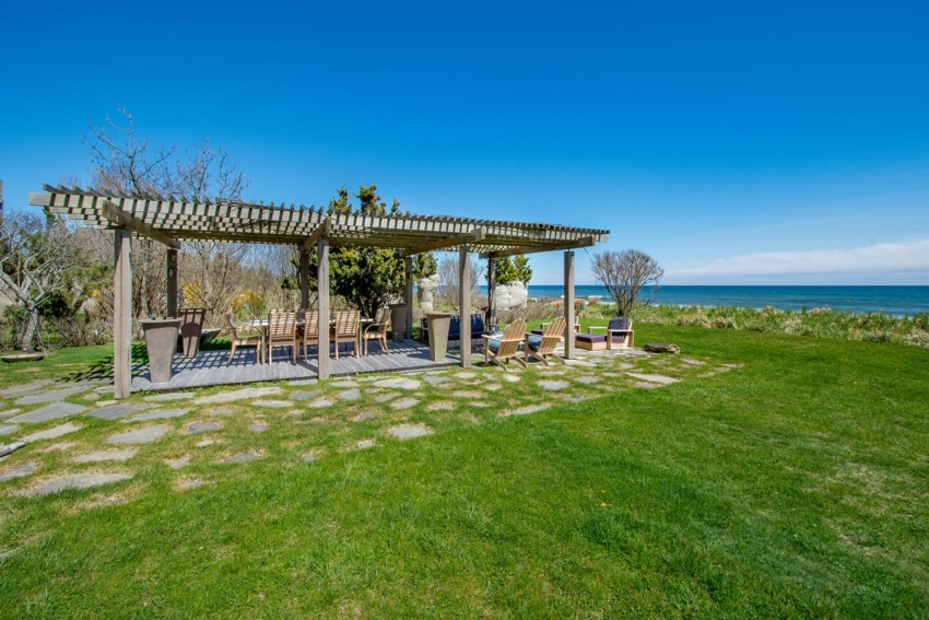 Pergola with seating on a grassy lawn overlooking the ocean under a clear blue sky