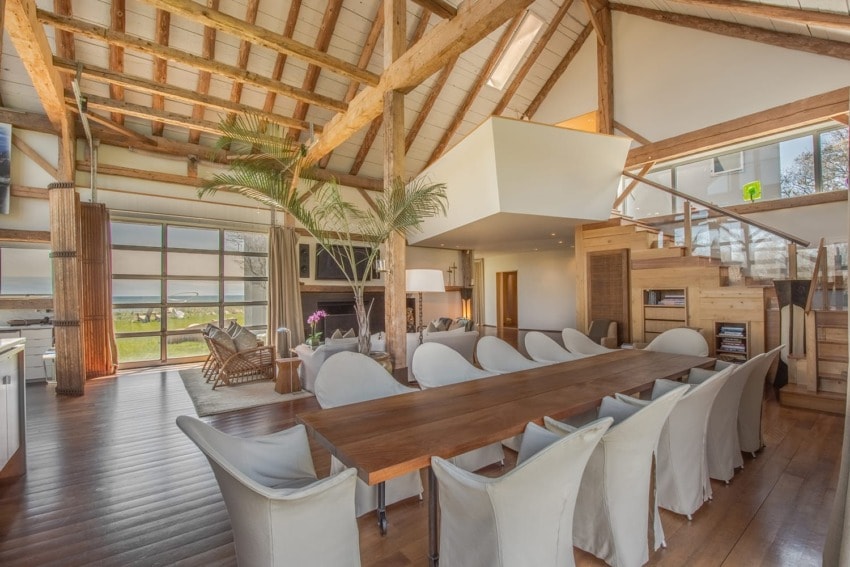Spacious open-plan living area with wooden beams, large dining table, modern furniture, and a view of the outdoors.