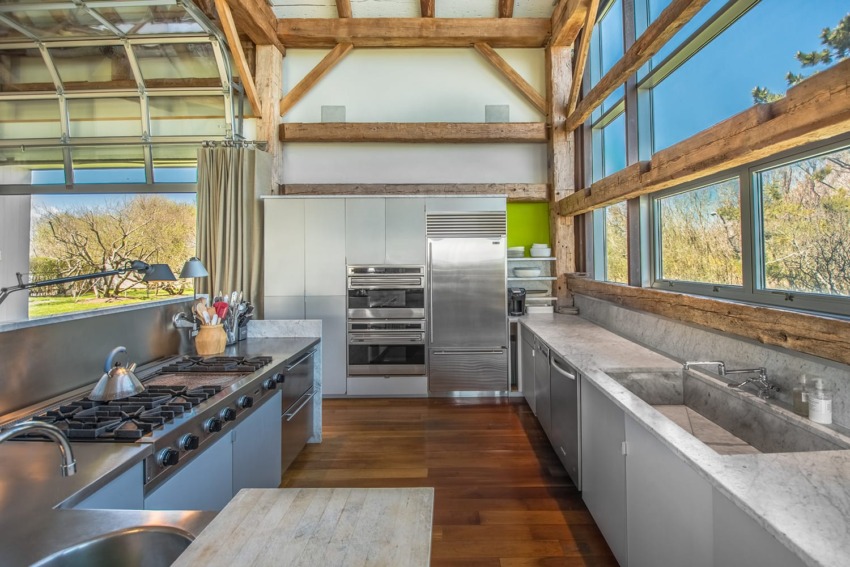 Spacious modern kitchen with stainless steel appliances, large windows, exposed wooden beams, and hardwood floors.