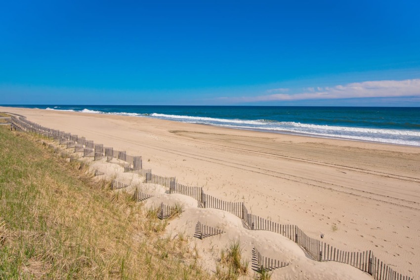 A sandy beach with ocean waves, wooden fences, and a clear blue sky in the background.