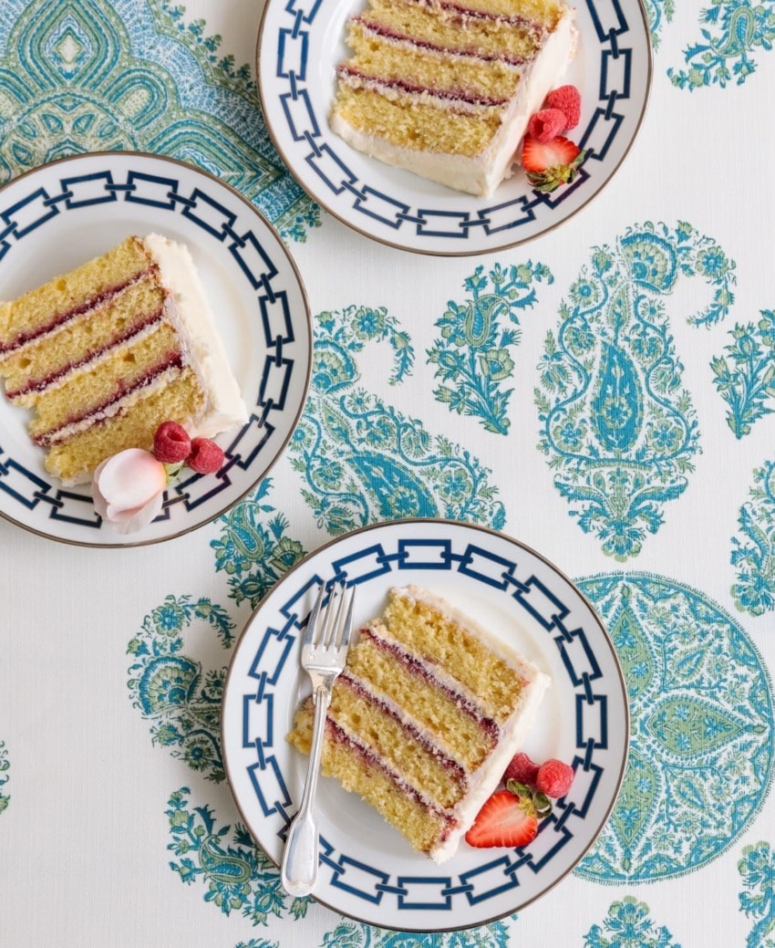 Three slices of layered cake with cream and berries on blue-patterned plates and a matching tablecloth.