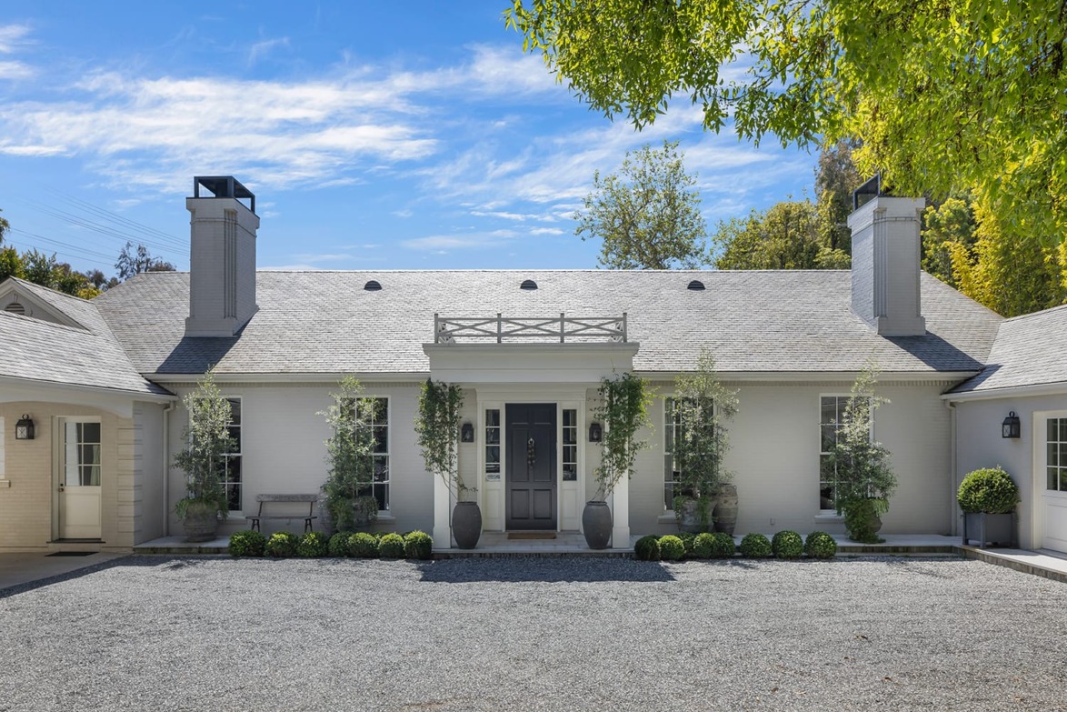 Front view of a modern single-story house with a gray roof, symmetrical windows, and trees framing the entrance.