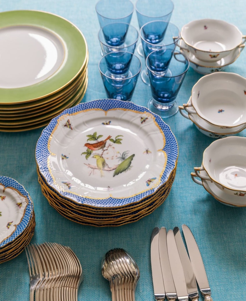 Elegant table setting with stacked decorative plates, blue glasses, and neatly arranged silverware on a blue tablecloth