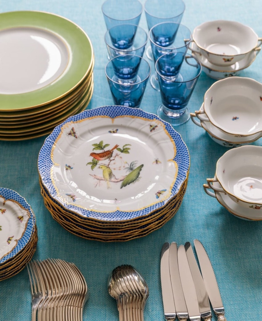 Elegant table setting with stacked decorative plates, blue glasses, and neatly arranged silverware on a blue tablecloth