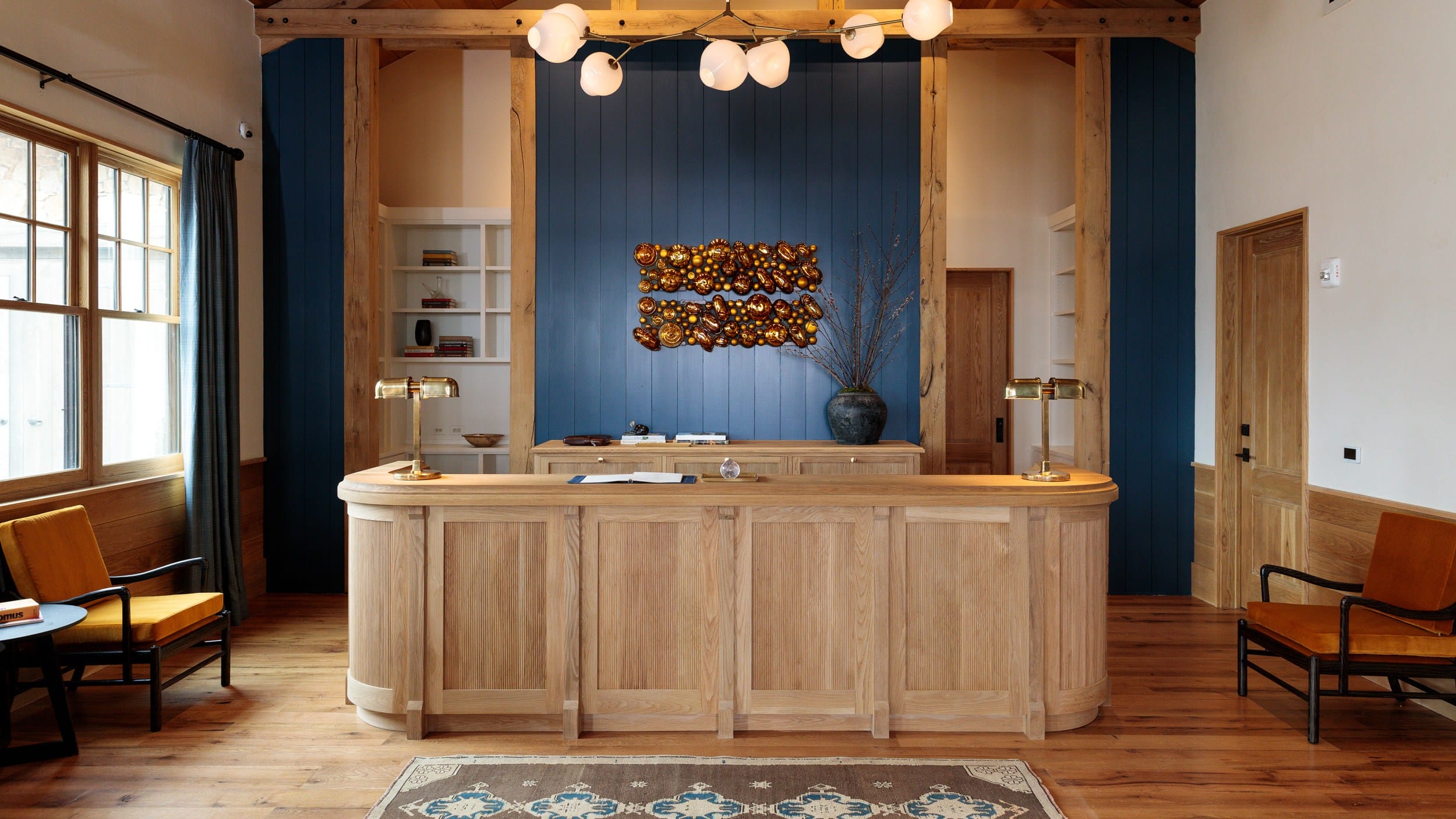 Hotel lobby with a wooden reception desk, blue accent wall, modern lighting, and cozy seating area.