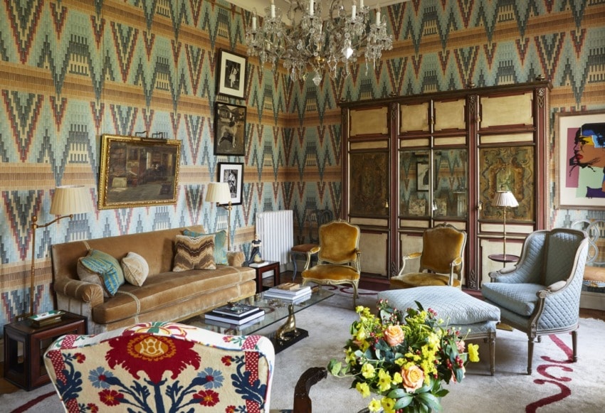 Eclectic living room with vintage furniture, colorful patterns, chandelier, and vibrant floral arrangement on the table.