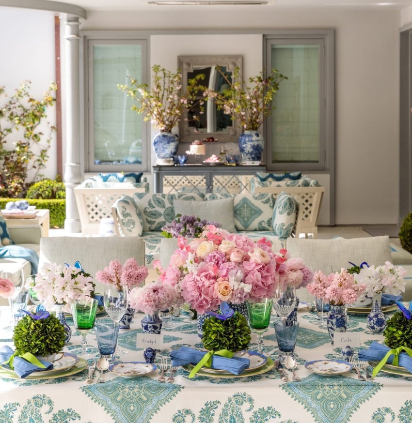 Elegant outdoor dining setup with floral arrangements, blue patterned plates, and green accents on a decorated table.