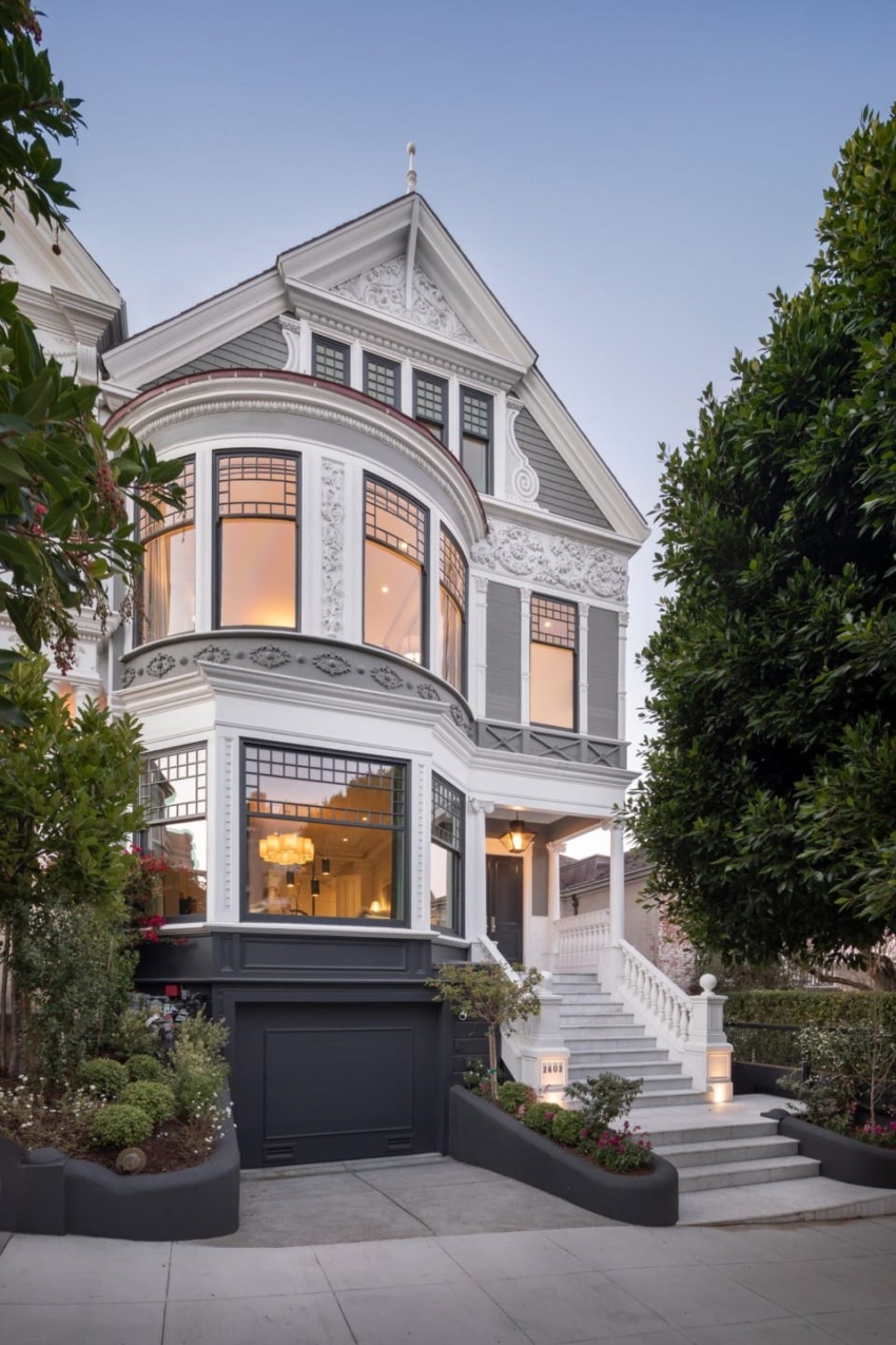 Victorian-style house with ornate details, large bay windows, and landscaped front yard at dusk.