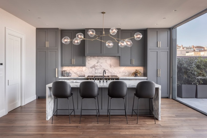Modern kitchen with gray cabinets, marble countertops, and stylish lighting fixture over a central island with bar stools.