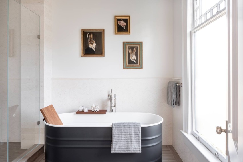 Modern bathroom with a black tub, wooden board, gray towel, and framed rabbit portraits on the wall above.