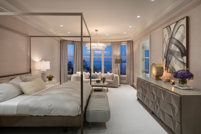 Luxurious bedroom with a four-poster bed, elegant decor, a seating area by a large window, and modern artwork on the wall.