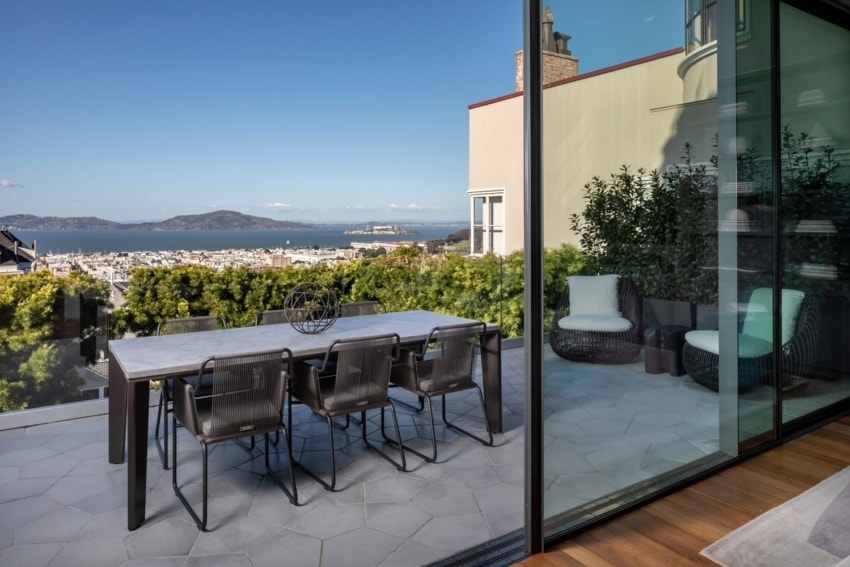 Rooftop patio with a dining table and chairs overlooking a cityscape and distant hills under a clear blue sky.