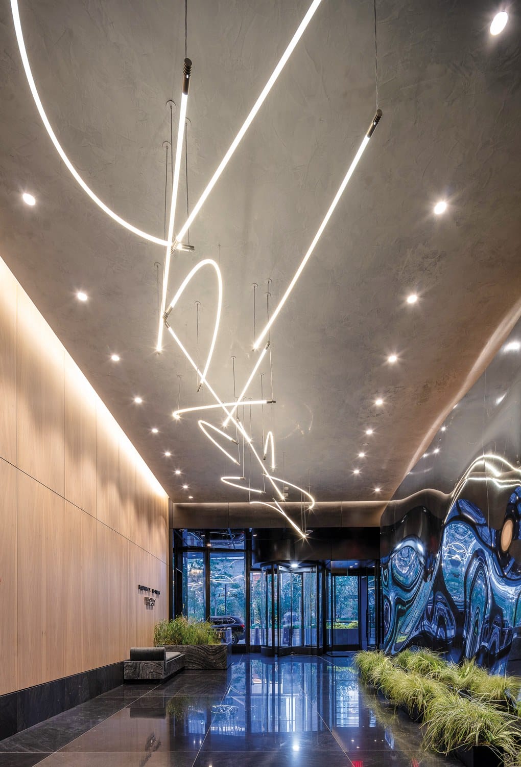 Modern lobby with abstract lighting, shiny marble floors, wood-paneled walls, and artistic wall decor near a glass entrance.