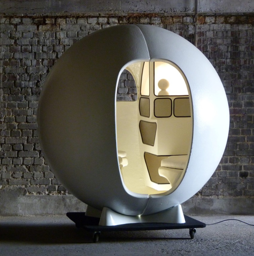 Futuristic egg-shaped pod with interior seating and lighting set against an industrial brick wall backdrop.