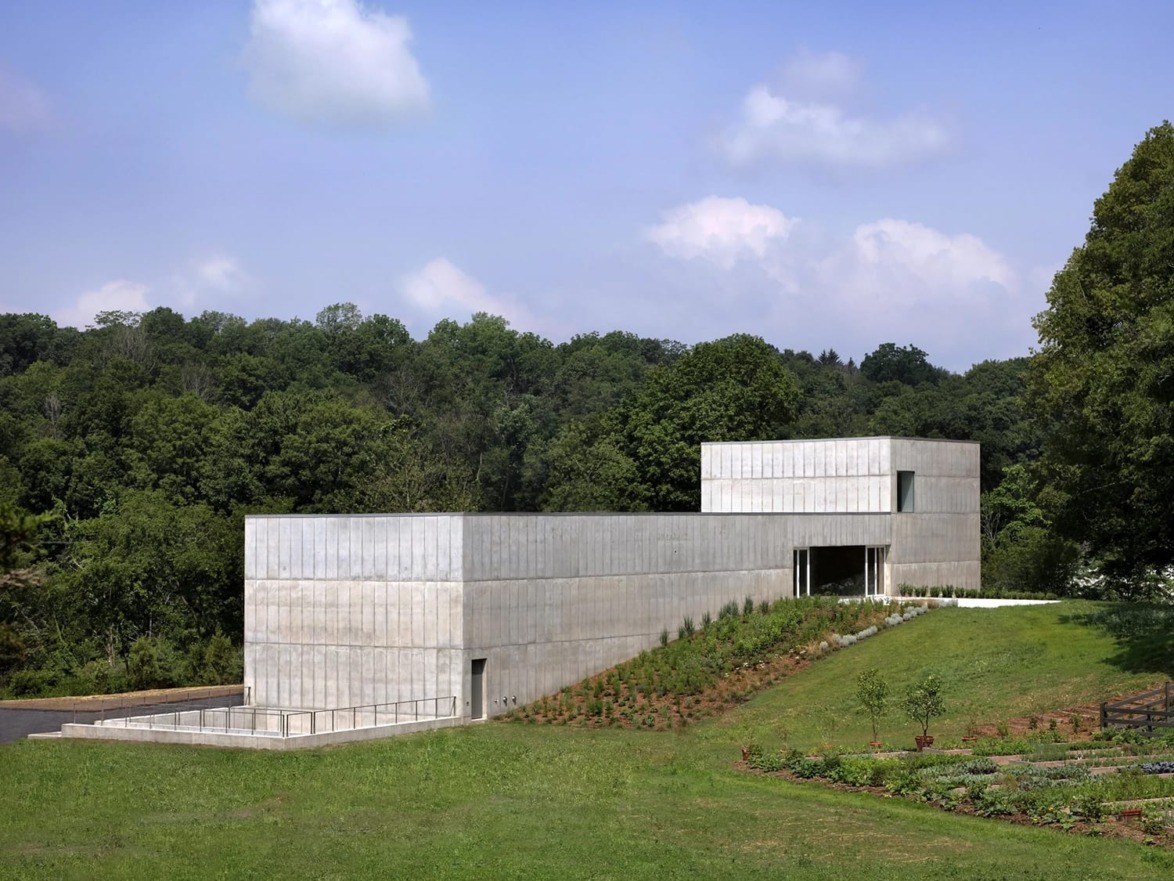 Modern concrete building surrounded by lush greenery and clear blue sky in a serene landscape setting.