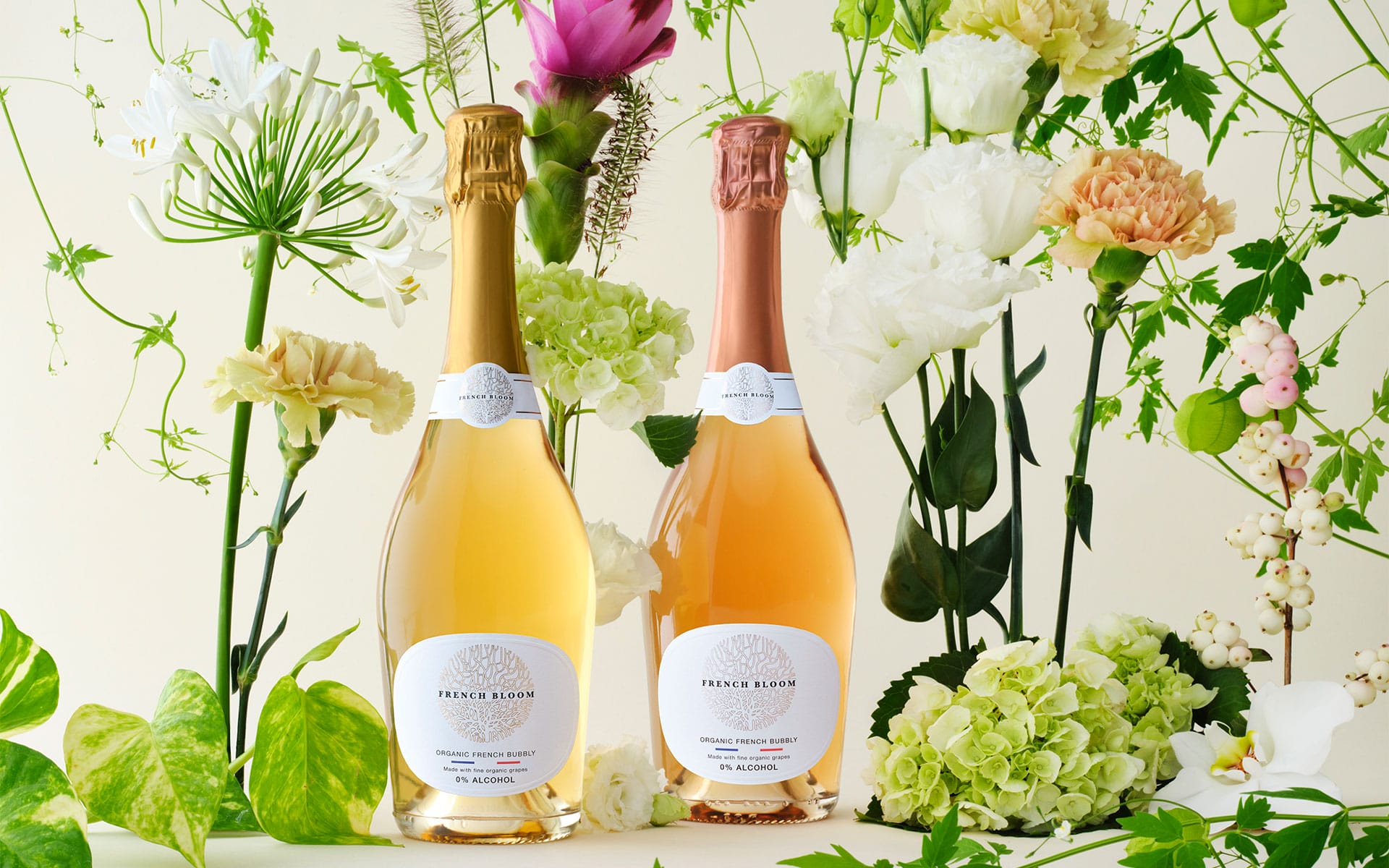 Two bottles of sparkling wine on a table surrounded by various colorful flowers and greenery.