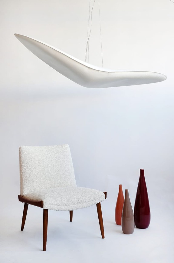 Modern white chair next to vases of varying colors and a sleek, abstract white hanging light fixture.