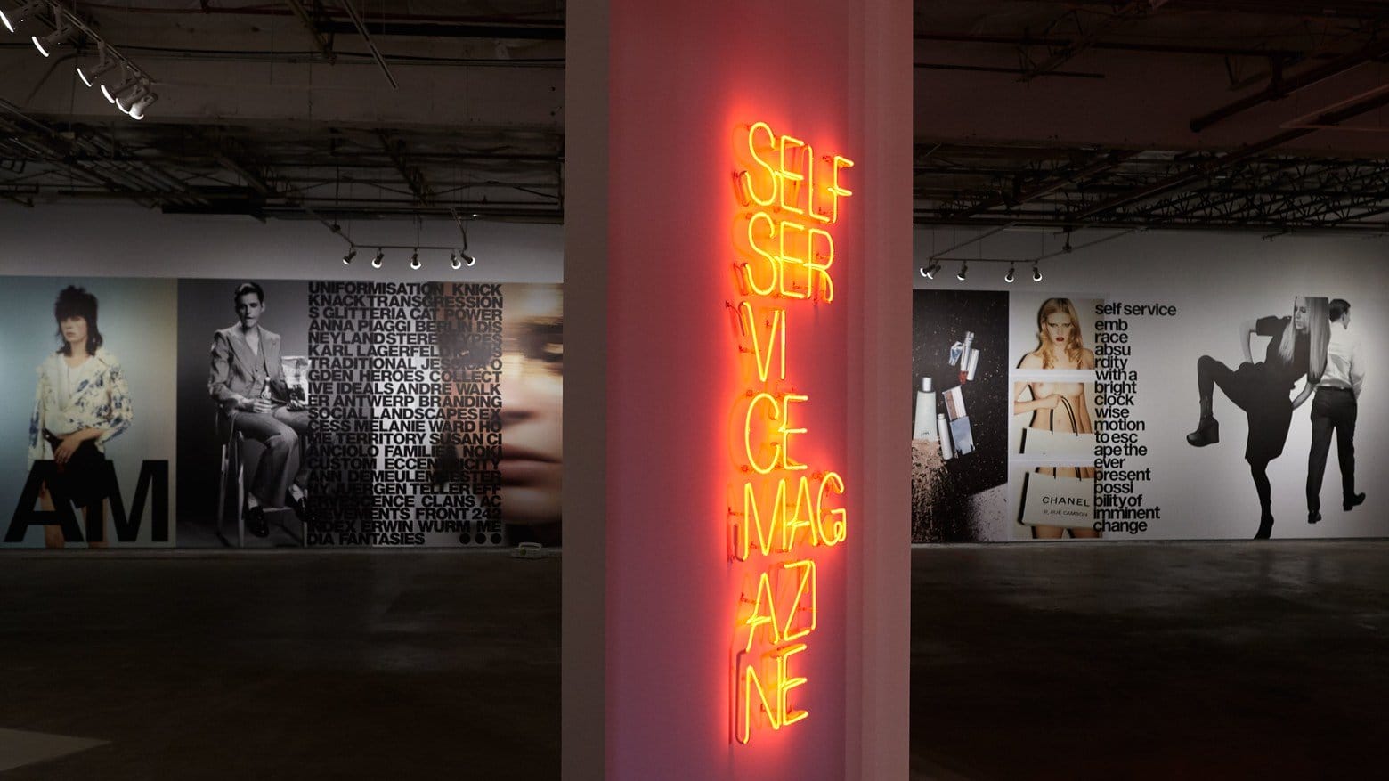 Gallery exhibition with neon sign "Self Service Magazine" on pillar, surrounded by fashion-themed images and text.