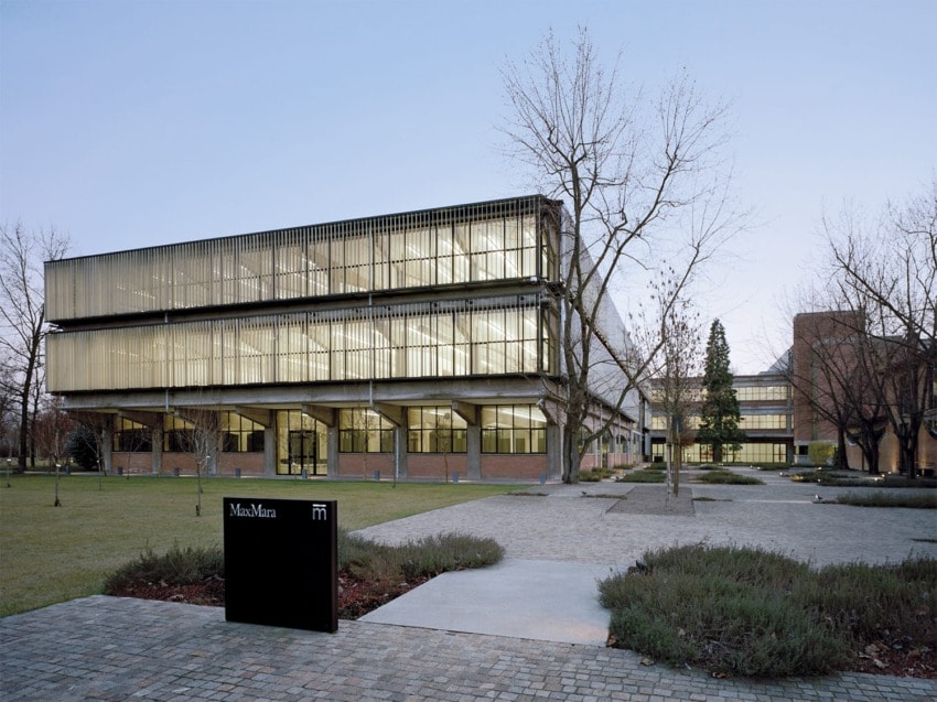 Modern building with glass facade surrounded by trees and pathway at dusk.