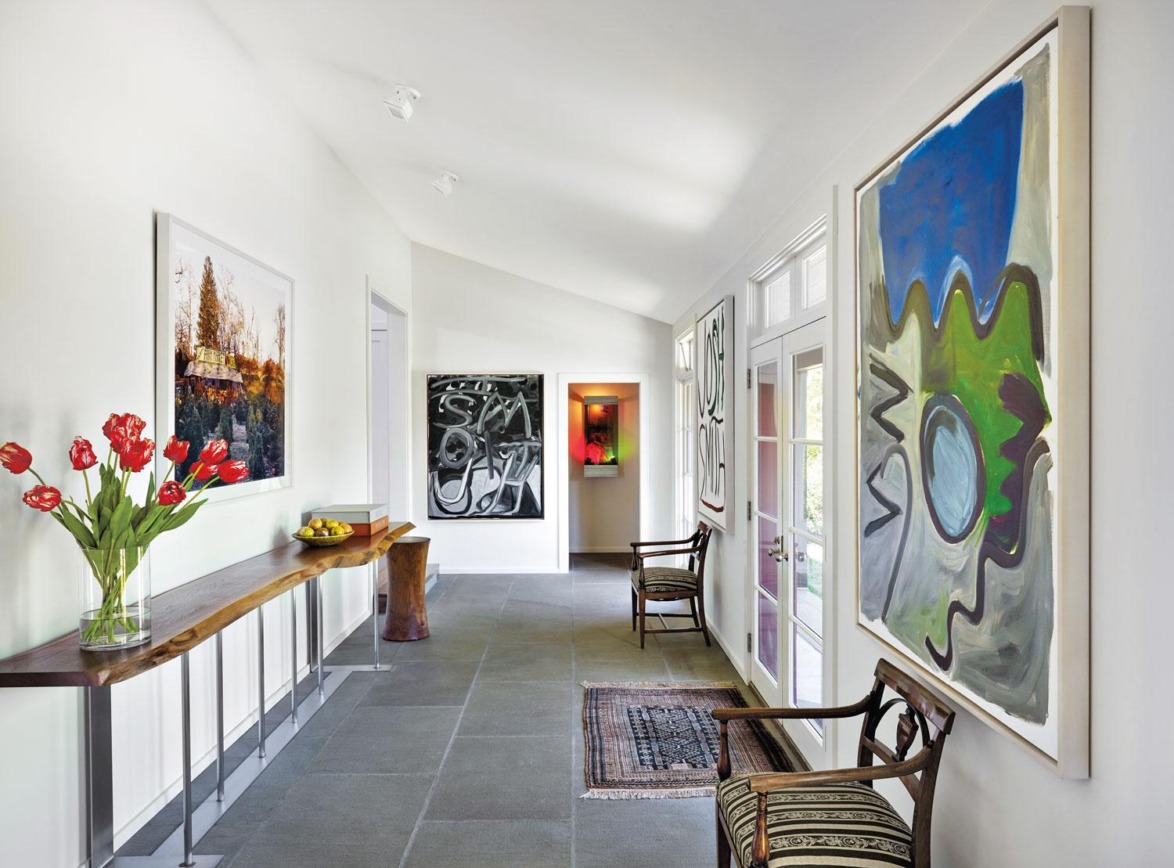 Modern art-filled hallway with large paintings, a wooden bench, tulips in a vase on a console table, and a carpet runner.