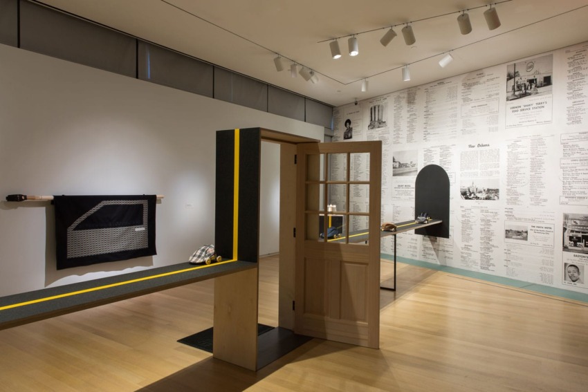 Modern art gallery interior with wooden door installation, display tables, and wall-mounted text and images.