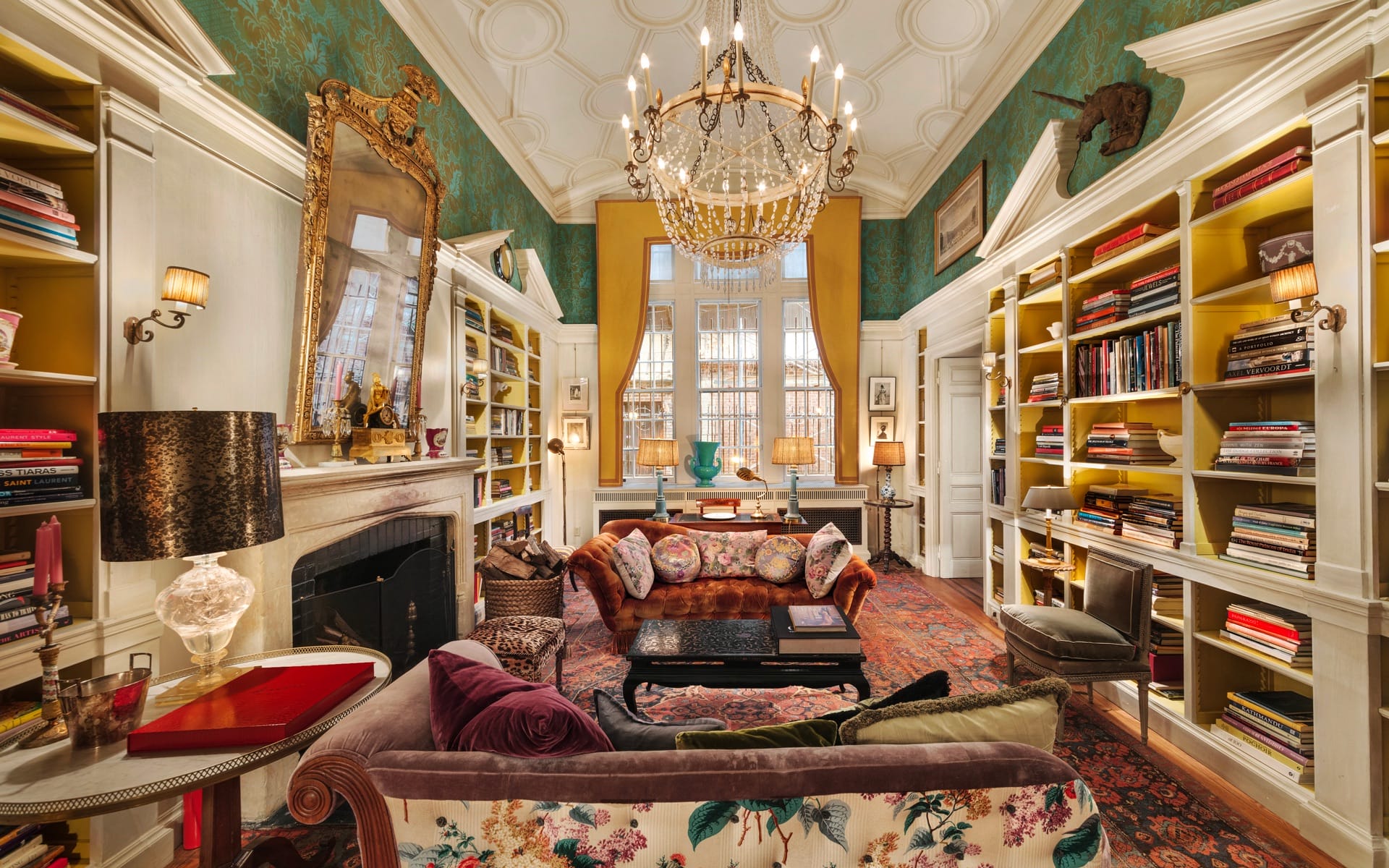 Luxurious living room with chandelier, patterned sofas, large mirror, bookshelves, and decorative fireplace.