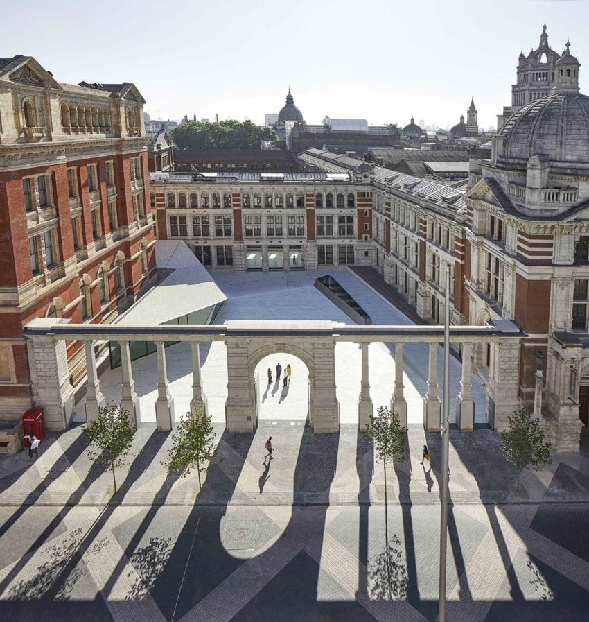 Aerial view of a historic courtyard with architectural columns, shadows, and people walking.