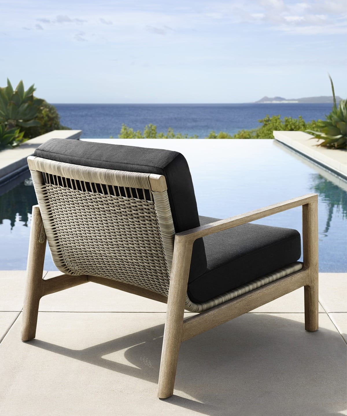 Outdoor chair with woven backrest overlooking an infinity pool and ocean view.